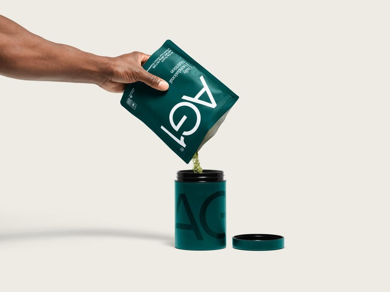 Hand pouring AG1 Daily Foundational Nutrition greens powder from pouch into AG1 storage canister